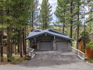 Nestled amongst tall pine trees, this modern home features a striking gray metal roof and siding, complemented by a spacious two-car garage.
