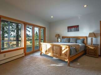 Experience serene living in this charming bedroom featuring a beautiful wooden sleigh bed and large windows that offer breathtaking views of the surrounding nature.