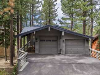 Nestled among tall pine trees, this charming home features a modern gray exterior with a sleek metal roof.