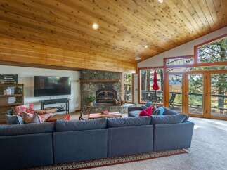 Experience breathtaking views from this stunning living room, featuring a grand stone fireplace and a vaulted wood-paneled ceiling.