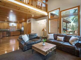 Experience rustic charm in this spacious living area, featuring a beautiful wood-paneled ceiling and a cozy seating arrangement centered around a rustic coffee table.