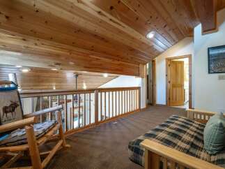 Experience rustic charm in this loft area, featuring a cozy rocking chair with a moose-themed cushion and a plaid futon perfect for relaxing.