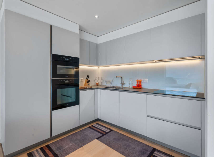 Experience modern living in this sleek, minimalist kitchen featuring integrated Miele appliances, including stacked ovens for ultimate culinary convenience.