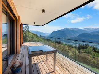Experience breathtaking mountain vistas from this stunning modern balcony, featuring a sleek glass railing and a stylish outdoor table.