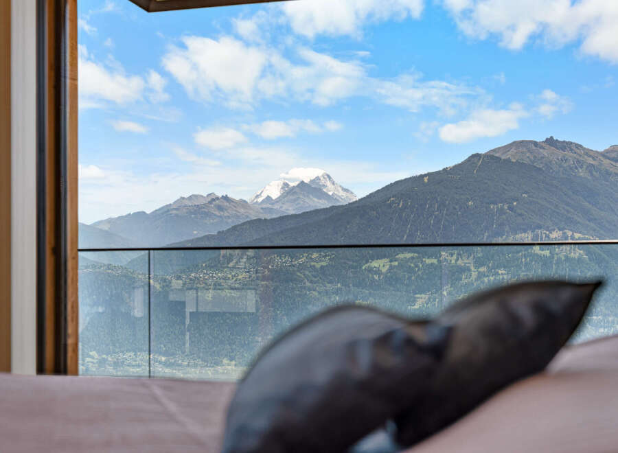Experience breathtaking panoramic views from this stunning property, featuring a modern glass balcony overlooking a picturesque valley and snow-capped mountains.