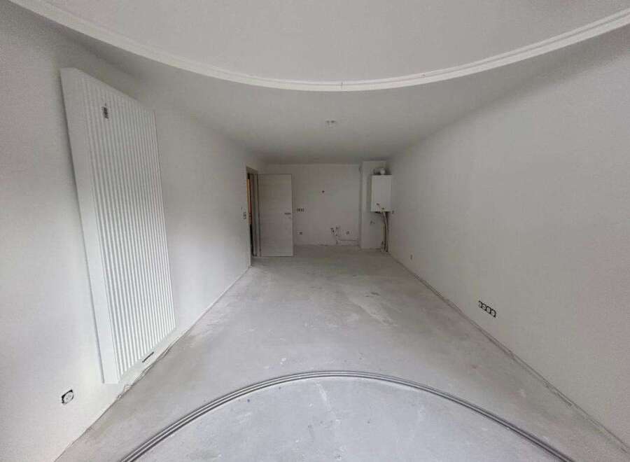 This unfinished room features a large vertical radiator on the left wall and a gas boiler mounted on the right wall.