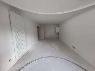 This unfinished room features a large vertical radiator on the left wall and a gas boiler mounted on the right wall.