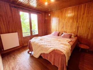 Experience rustic charm in this cozy bedroom featuring warm wood paneling throughout and a large window offering scenic views.