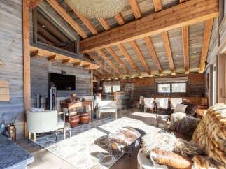 Experience rustic luxury in this stunning chalet living room, featuring exposed wooden beams, a stone fireplace, and plush, animal-print seating.