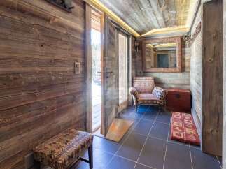 Step into a charming rustic entryway featuring warm wooden walls and ceiling, complemented by a cozy armchair and a decorative bench.