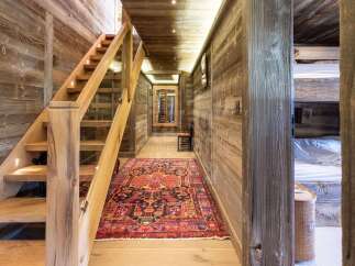 Experience rustic charm in this mountain chalet hallway, featuring a beautiful wooden staircase with integrated lighting and a vibrant Persian rug.