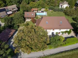 Discover this expansive property featuring a main residence with a classic tiled roof and multiple windows, complemented by a separate guest house and a refreshing swimming pool.