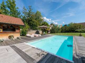 Enjoy ultimate relaxation in this backyard oasis featuring a sparkling swimming pool and a charming wooden bar area, perfect for entertaining.