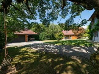 Discover this charming property featuring a modern wooden house and a convenient garage, set amidst lush greenery and mature trees.