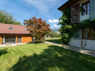 Discover this charming property featuring a modern wooden-clad building with a red tiled roof and a traditional house adorned with climbing ivy and rustic shutters.