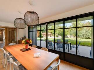Experience seamless indoor-outdoor living with this stunning dining area, featuring a large wooden table and chairs overlooking a lush backyard.