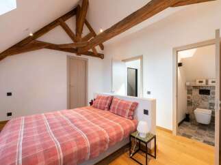 Experience rustic charm in this attic bedroom featuring exposed wooden beams and a cozy plaid comforter.