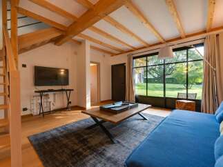 Experience modern living in this spacious room featuring exposed wooden beams and a large window overlooking a lush garden.