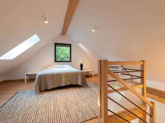 Discover this charming attic bedroom featuring a cozy bed with a plush throw, illuminated by natural light from a skylight and a window overlooking lush greenery.
