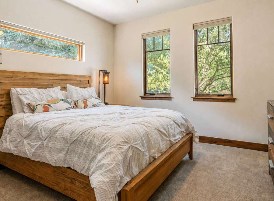 Experience serene living in this charming bedroom, featuring a rustic wooden bed frame and a large horizontal window offering picturesque views of lush greenery.