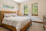 Experience serene living in this charming bedroom, featuring a rustic wooden bed frame and a large horizontal window offering picturesque views of lush greenery.