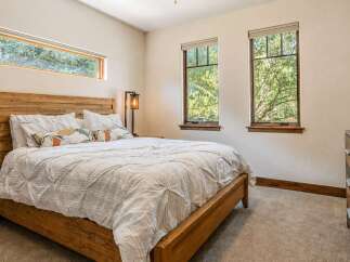 Experience serene living in this charming bedroom, featuring a rustic wooden bed frame and a large horizontal window offering picturesque views of lush greenery.