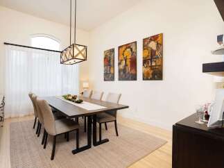 This elegant dining room features a spacious wooden table set for six, complemented by a neutral-toned rug and a striking modern chandelier.