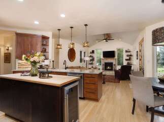 Experience luxury living in this open-concept home featuring a gourmet kitchen with a large island and wine fridge, seamlessly flowing into a cozy living area with a stone fireplace.