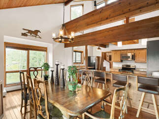 Experience rustic charm in this spacious dining and kitchen area, featuring a large wooden dining table with ornate chairs and a cozy breakfast bar with leather stools.