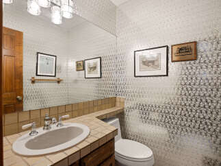 This powder room features a stylish vanity with a tiled countertop and backsplash, complemented by a large mirror reflecting the elegant wallpaper.