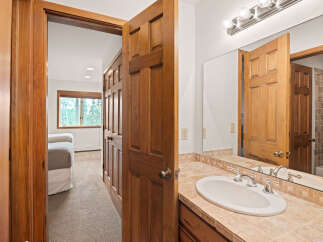 Step into a charming bathroom featuring a spacious vanity with a tiled countertop and a clean white sink, complemented by a large mirror reflecting the warm wooden doors.