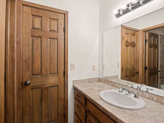 This bathroom features a beautiful wooden door and a vanity with a tiled countertop and a white sink.