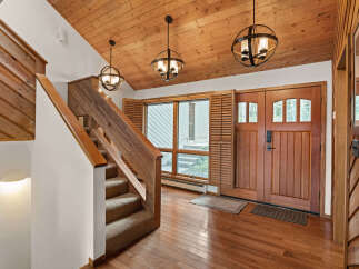 Step into a warm and inviting entryway featuring a beautiful wooden staircase with carpeted treads and a rustic wood accent wall.