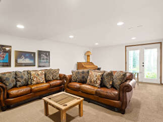 This inviting basement living area features two plush leather sofas adorned with decorative pillows, centered around a unique backgammon coffee table.