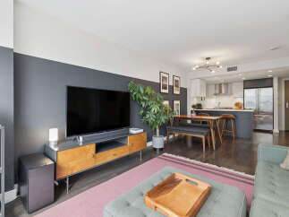 This modern living and dining area features a sleek entertainment center with a large flat-screen TV, complemented by a stylish dining set with bench seating and bar stools.