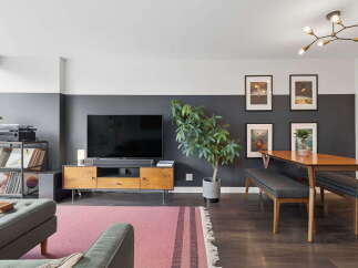 This stylish living and dining area features a modern entertainment center with a large TV, complemented by a warm wooden dining table and comfortable upholstered benches.