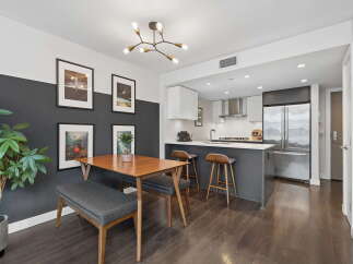 This modern dining area and kitchen features a stylish dining set with a wooden table and upholstered bench, complemented by a striking geometric chandelier.