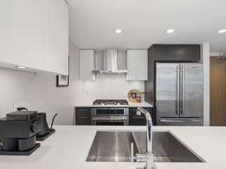 Experience modern living in this sleek kitchen, featuring stainless steel appliances including a double-door refrigerator and a gas range with a matching hood.