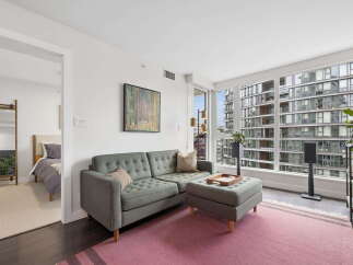 Experience modern urban living in this stylish condo featuring a spacious living area with a tufted sofa and ottoman, complemented by a large pink rug.