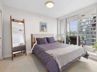 Experience modern urban living in this stylish bedroom, featuring a comfortable bed with plush purple bedding and a cozy throw.
