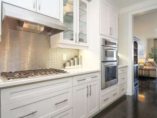 Experience modern luxury in this stunning kitchen, featuring sleek white cabinetry, a gleaming stainless steel backsplash, and top-of-the-line stainless steel appliances including a double oven and gas range.