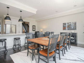 This spacious open-concept dining and kitchen area features a large wooden dining table with seating for eight, complemented by a sleek white island with bar stools.