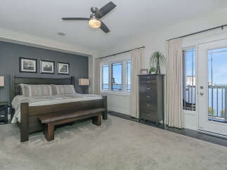 Experience luxurious waterfront living in this stunning master bedroom, featuring a king-size bed with elegant bedding and a rustic wooden bench.