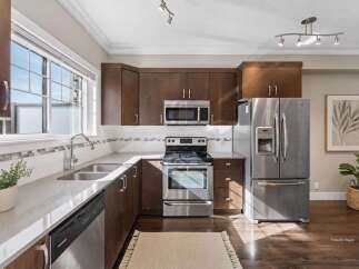 Discover this beautifully appointed kitchen featuring rich, dark wood cabinetry complemented by sleek stainless steel appliances, including a modern microwave and a spacious refrigerator with a water dispenser.