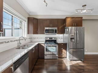 Discover this beautifully appointed kitchen featuring rich, dark wood cabinetry complemented by sleek stainless steel appliances, including a modern microwave and a spacious refrigerator with a water dispenser.
