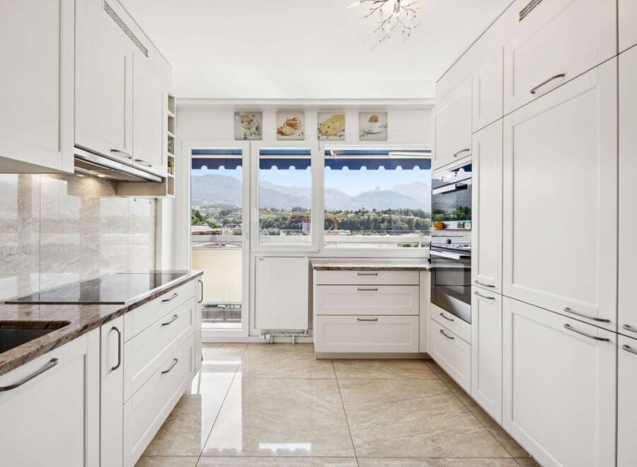 Experience breathtaking mountain views from this modern kitchen, featuring sleek white cabinetry and granite countertops.