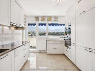 Experience breathtaking mountain views from this modern kitchen, featuring sleek white cabinetry and granite countertops.