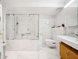 This modern bathroom features a sleek bathtub with a glass enclosure, a wall-mounted toilet, and a spacious vanity with a large sink.