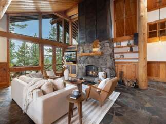 Experience breathtaking mountain views from this stunning living room, featuring a grand stone fireplace and expansive windows.