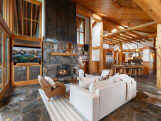 Experience rustic luxury in this stunning log cabin living room, featuring a grand stone fireplace and a large TV entertainment center.